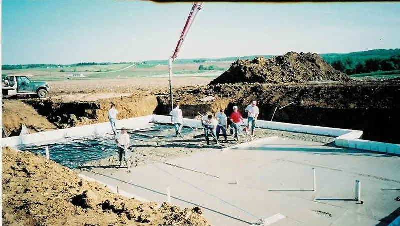 Crew placing a basement floor slab inside new foundation walls with the pump boom above