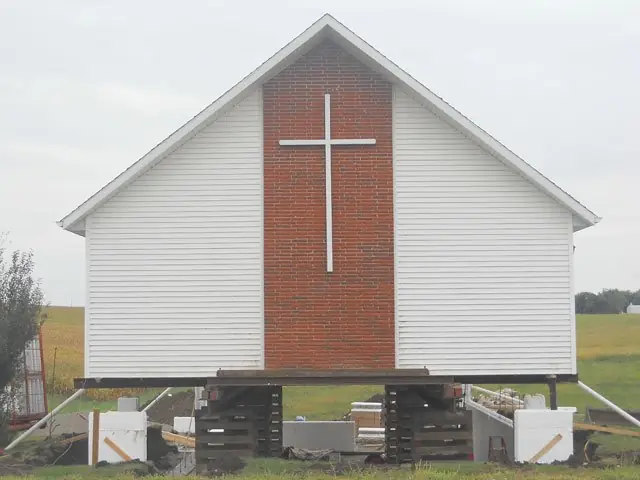 White church with brick front and cross, lifted on cribbing for a new foundation