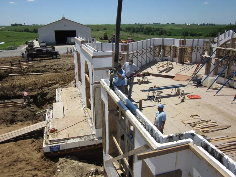 Crew on scaffolding filling insulated concrete form walls from the pump hose